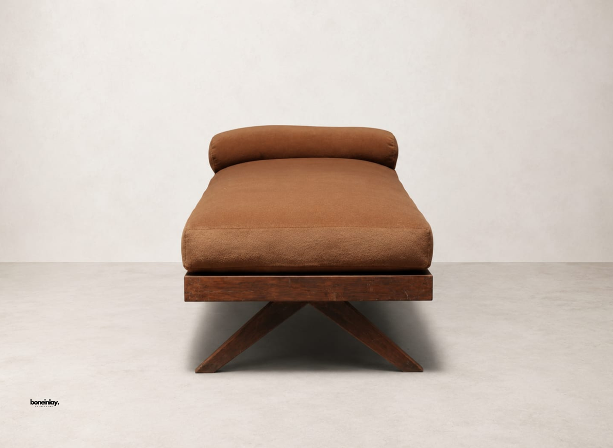 End profile view of a handmade wooden daybed highlighting the sturdy cross-leg architecture, dark wooden base, and plush brown cushion. This versatile artisan lounge furniture piece combines minimalist aesthetics with cozy lounging for upscale US spaces.