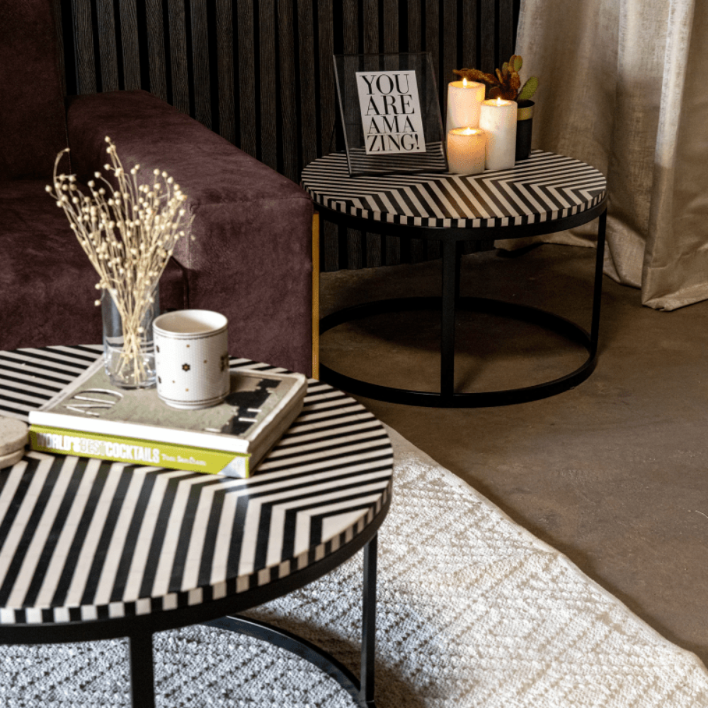 Black and white bone inlay round coffee table and side table set styled in a warm cozy living room with candles and books, luxury artisan handcrafted furniture