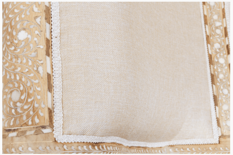 Overhead close-up of linen seat cushion on traditional wood inlay chaise lounge with floral bone inlay frame on both sides