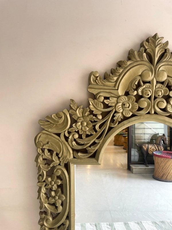 Botanical wood looking glass in a gold-toned finish, corner detail view showing carved flowers and curling leaves.