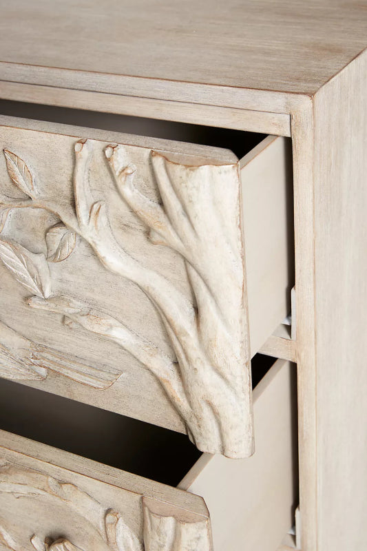 Close-up of the washed-grey wood dresser, showing hand-carved birds and leafy branches on its drawer front.