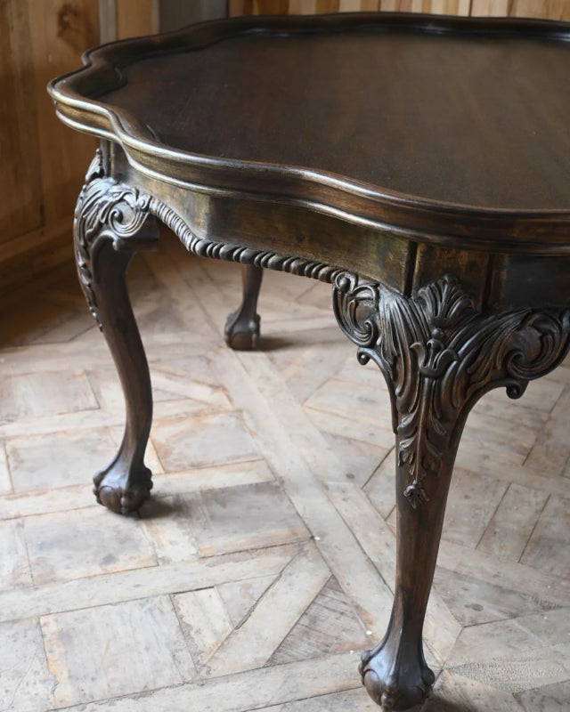 Carved wood accent table in an edge detail view, focusing on the shaped apron beneath the round tabletop.
