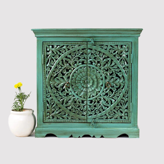 Floral carved wood small cupboard in distressed emerald green, front view showing two doors with a circular floral medallion.