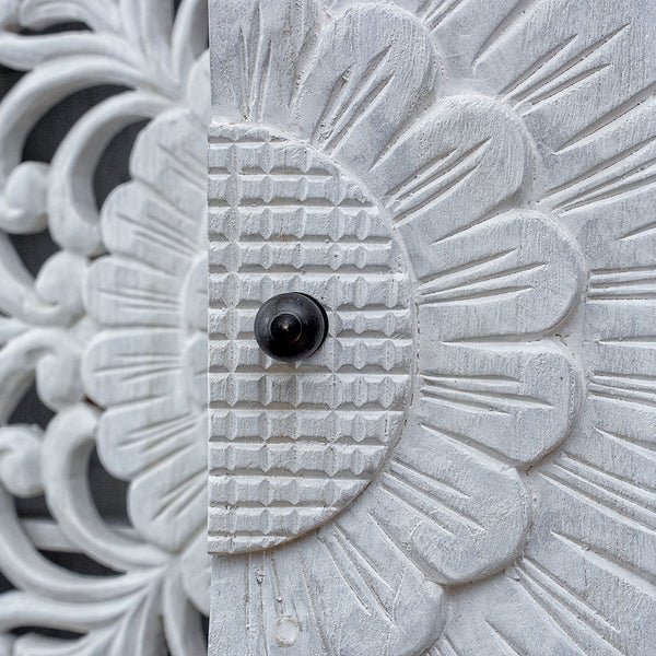 Floral door storage buffet in rustic wood, close-up of a dark round door knob against textured flower carving.