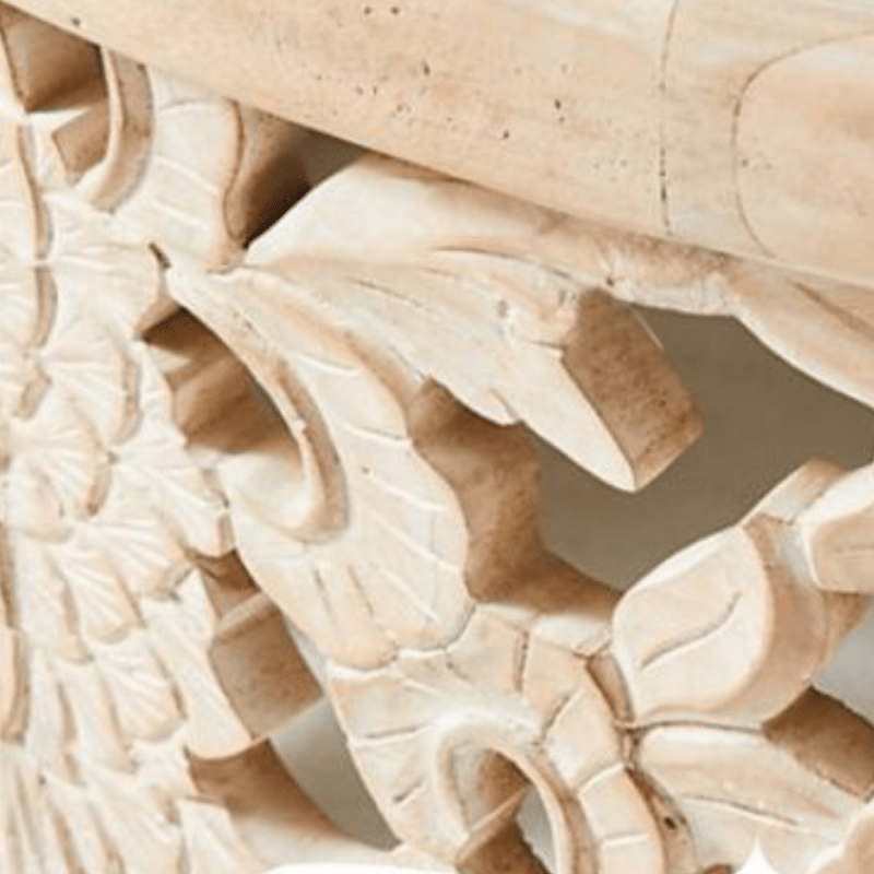 Hand-carved wood cocktail table in a light natural finish, edge detail view showing leaves beneath the top rim.