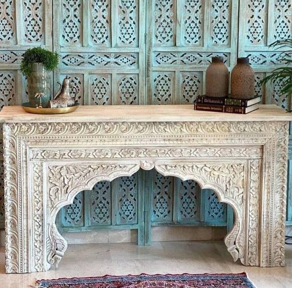 Hand carved wooden sofa table with a rustic finish, front view showing floral borders beneath plants and pottery.