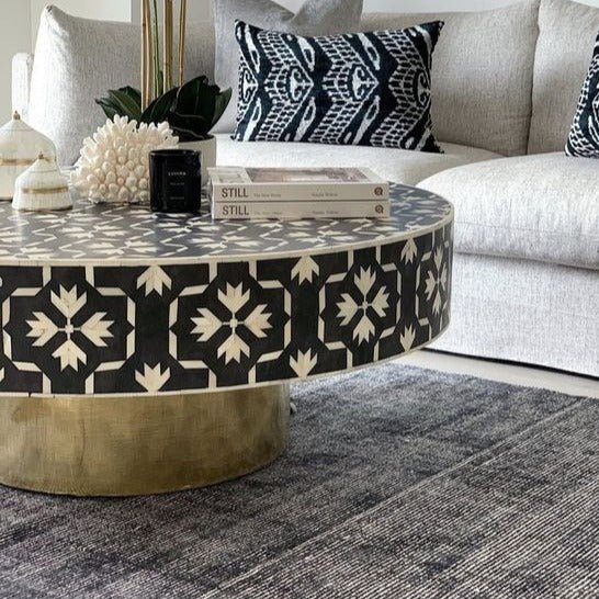 Handcrafted bone inlay mosaic coffee table with intricate black and white floral pattern and gold metal base, placed in a cozy living room styled with a grey sofa and decorative cushions