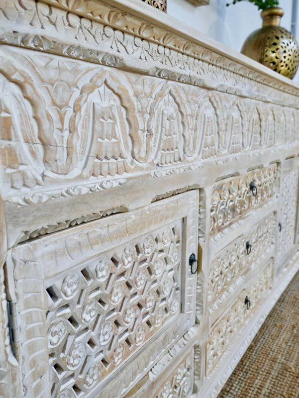 Geometric carved wood cabinet in a whitewashed finish, shown in an angled close-up of its patterned front panels.