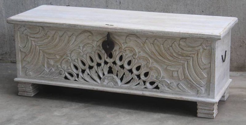 Rustic carved wooden trunk in solid wood, front view showing a dark right side handle and peacock carving above block feet.