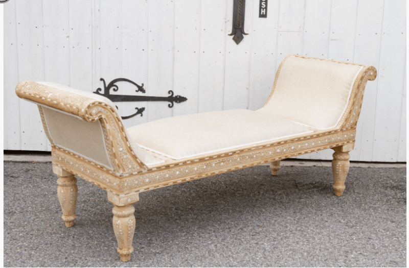 Traditional wood inlay teak chaise lounge at diagonal angle showing full length cream upholstered seat and ornate carved frame