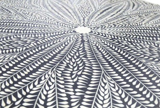 Close-up of ivory bone inlay leaves radiating from a floral center on the black dining tabletop.