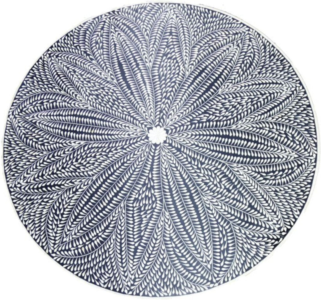 Top view of a round black dining tabletop with an intricate ivory bone inlay leaf pattern and floral center.