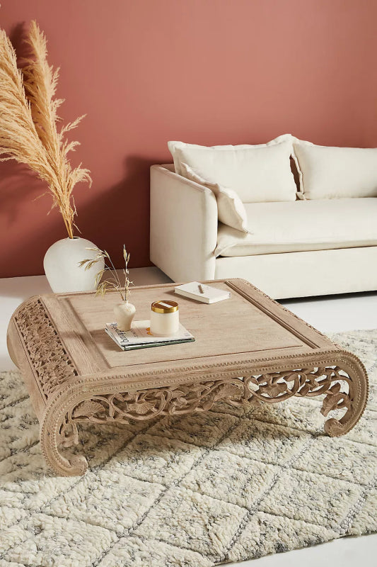 Ornate square coffee table in light-toned solid wood featuring intricate hand-carved scrolling floral patterns on its curved legs and apron.