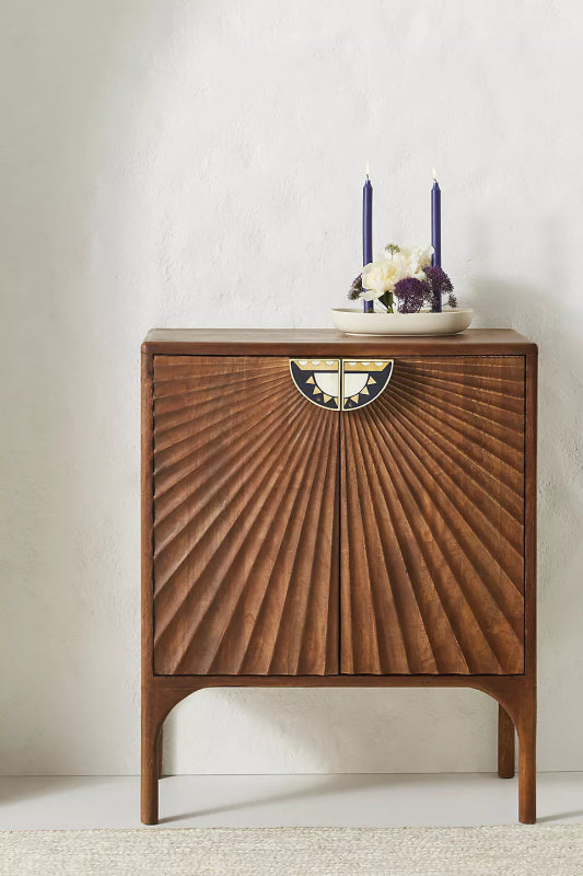 Warm-toned wood daybreak cabinet featuring dramatic, fan-like hand-carved fluted doors and decorative half-moon inlaid hardware on a sturdy, arched leg base.