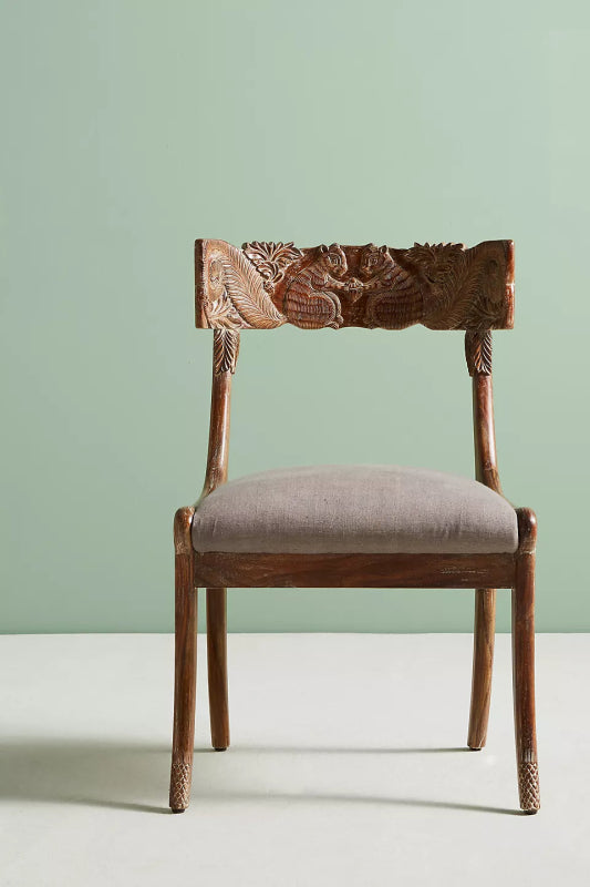 Fable dining chair in rich solid wood featuring an intricately hand-carved backrest with animal and floral motifs and a neutrally upholstered seat.