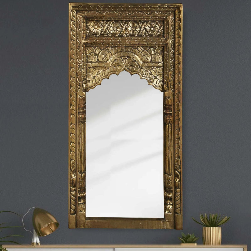Ornate Moorish arch wall mirror featuring an embossed brass foil clad frame with floral patterns and side columns against a dark grey wall.