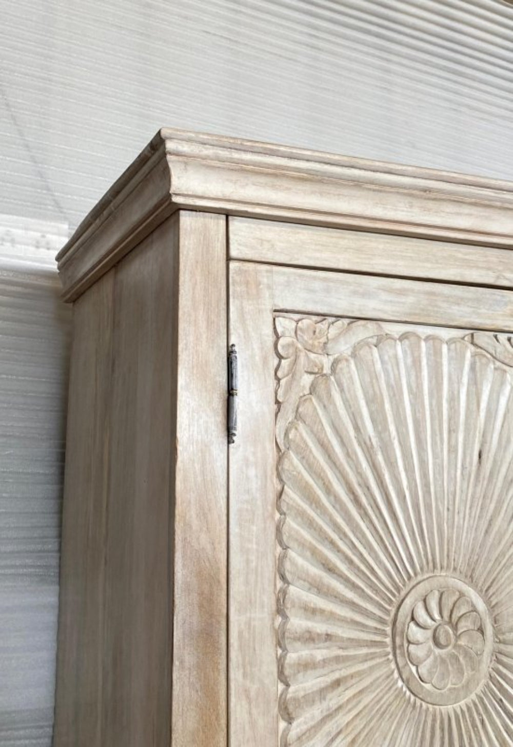 armoire in rustic solid wood, close-up of the corner detail with a sunburst carved motif.