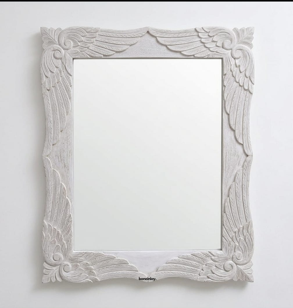 A rectangular wooden wall mirror from the Menagerie collection, featuring a carved frame with ornate wing and scrollwork patterns finished in distressed off-white and gold, shown against a plain white wall.