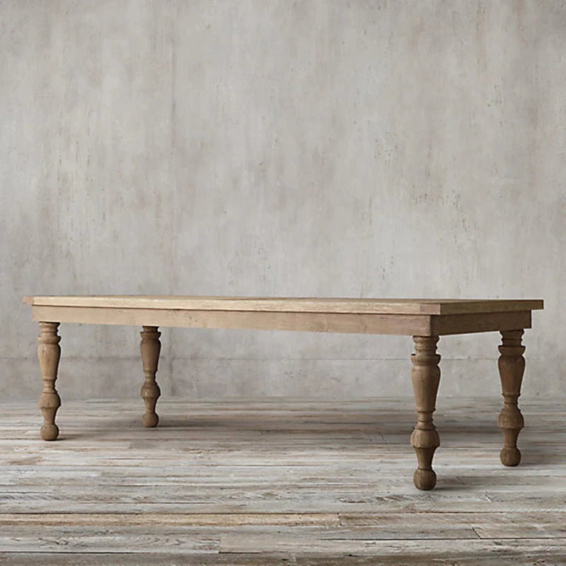 A luxury hand-carved solid wood dining table with thick baluster-turned legs and a natural light wood finish in a minimalist room setting.