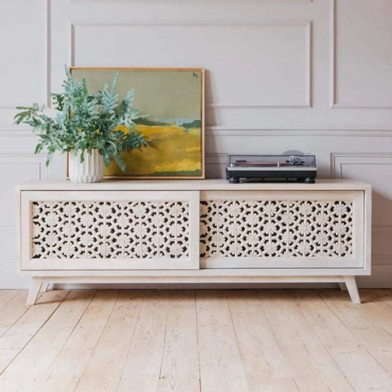 A wide Momoka media console made of white-washed hand-carved mango wood, featuring intricate floral lattice sliding doors and tapered Mid-Century legs.