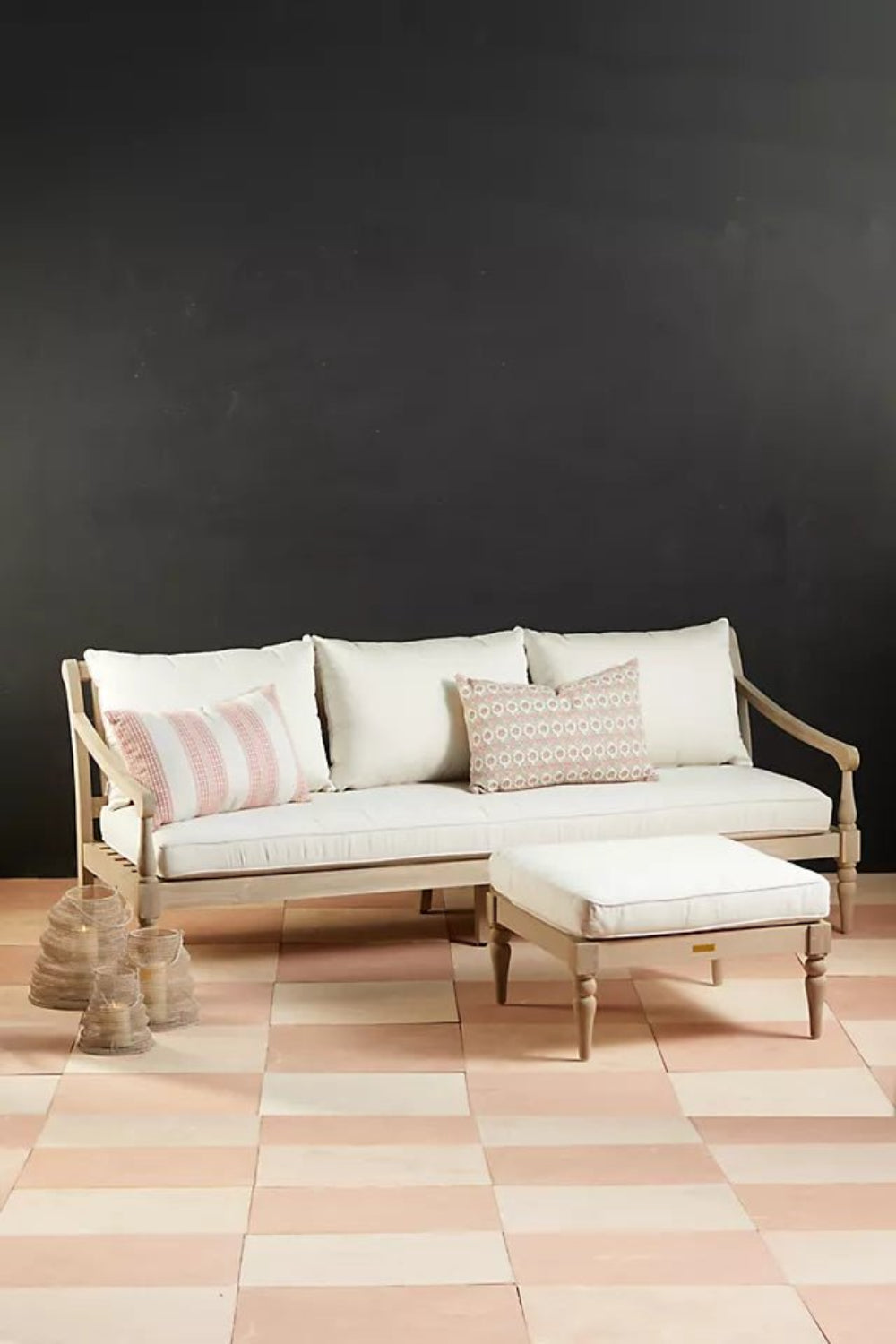 Cushioned wooden sofa with a solid frame, front view showing three back cushions and an ottoman against a dark wall.