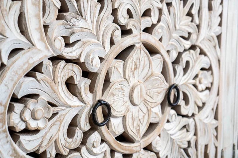 Floral ring-pull storage cabinet in rustic wood, close-up of carved door flowers with two dark circular handles.