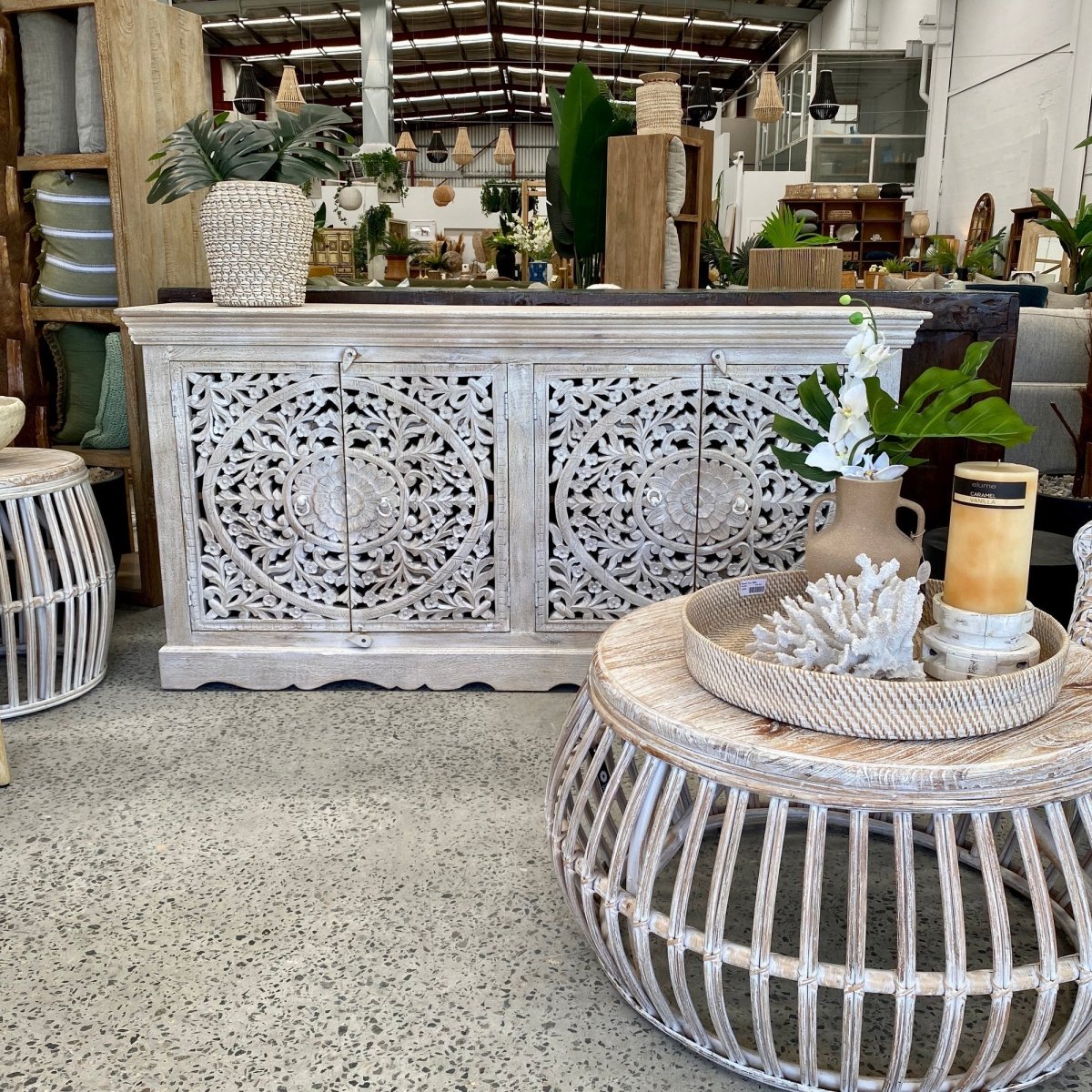Rustic openwork wood buffet with carved floral doors, front view behind a round table displaying flowers and a candle.