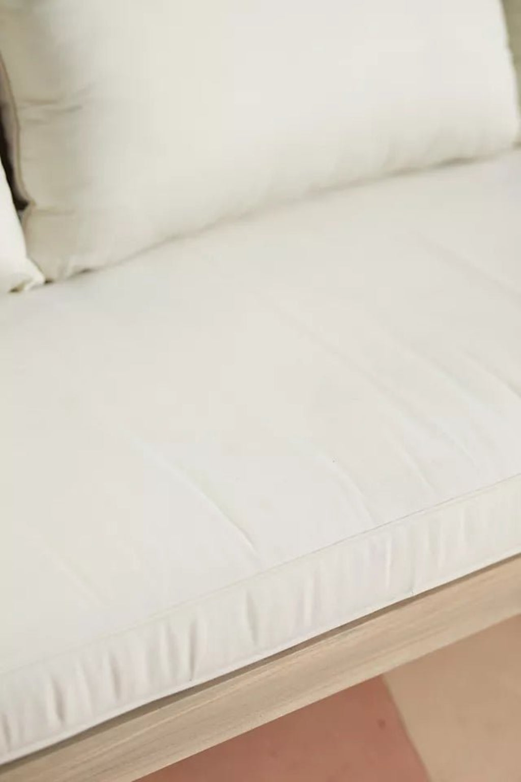 Upholstered wood settee with light fabric, edge detail view showing the seat cushion seam above the wooden front rail.