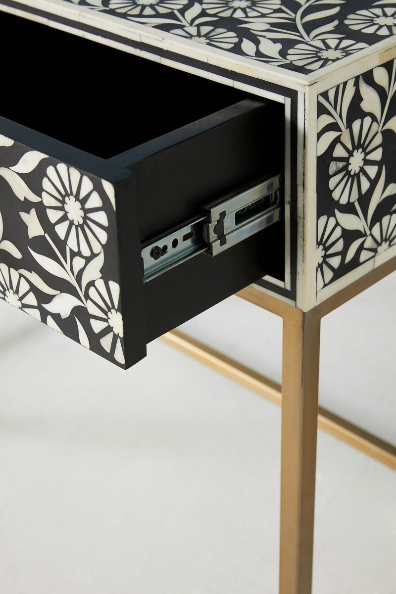Black bone inlay entry table in an open drawer view, showing one drawer pulled forward to reveal its interior, white floral inlay on the black drawer front, a brass knob, the remaining drawers, and the gold-toned base below.