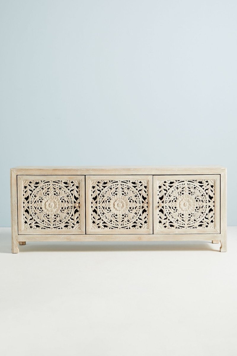 Three-door solid wood media console in a white-washed finish featuring intricate, open-work hand-carved floral medallions on each door panel.