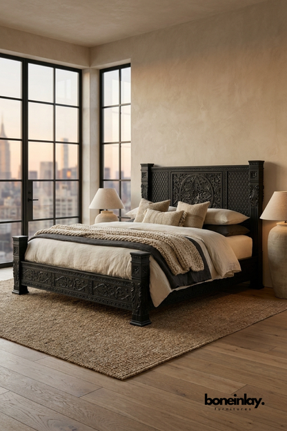 Black carved wood bed with detailed craftsmanship styled in a contemporary bedroom featuring oversized windows, warm neutral textiles, and a city skyline view.