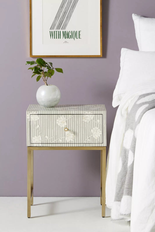 Ada grey and white floral stripe bone inlay nightstand with brass gold metal base styled in a serene luxury bedroom with white linen bedding and a ceramic vase with botanicals.