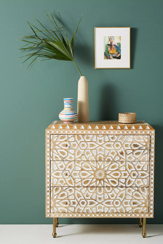 Close-up of Albaron three-drawer dresser featuring intricate hand-carved geometric star patterns in a white finish on natural mango wood with slim brass legs against a teal wall.