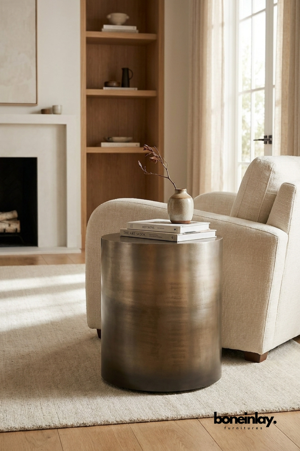 Minimalist cylindrical antique brass metal side table accent piece next to a cream armchair in a modern neutral living room .