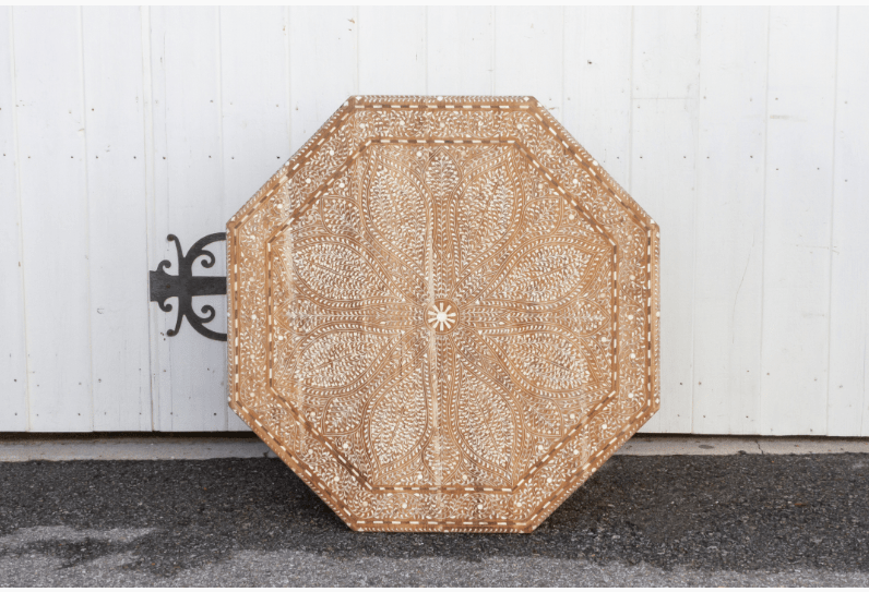 Top-down view of octagonal bone inlay coffee table surface featuring symmetrical floral mandala pattern with central star motif on teak wood.