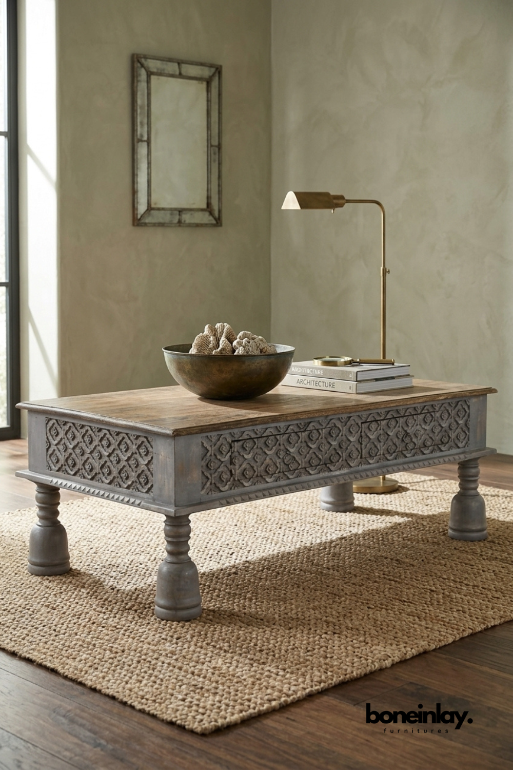 Weathered grey coffee table featuring a hand-carved diamond trellis pattern along the apron and turned bun feet. Natural wood tabletop contrasts with the distressed grey-washed base for rustic charm. Styled with a bronze bowl of coral and a brass reading lamp on a jute rug. A substantial statement coffee table for farmhouse and traditional living rooms.