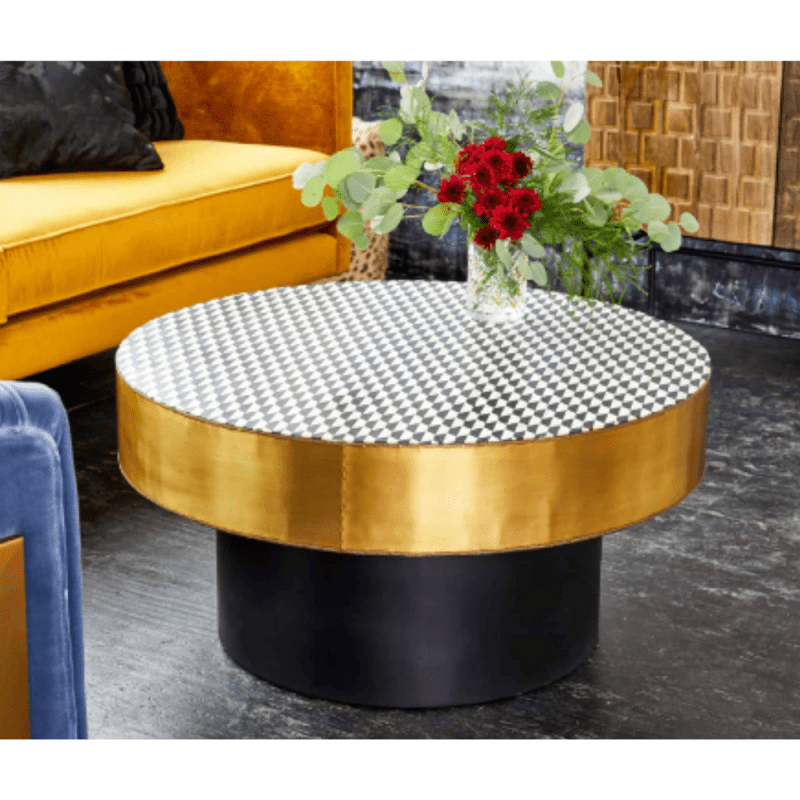 Three-quarter front view of a round bone inlay coffee table with a black and white diamond checkerboard top, gold metal rim, and black pedestal base, presenting the geometric tabletop and cylindrical support against a light background.