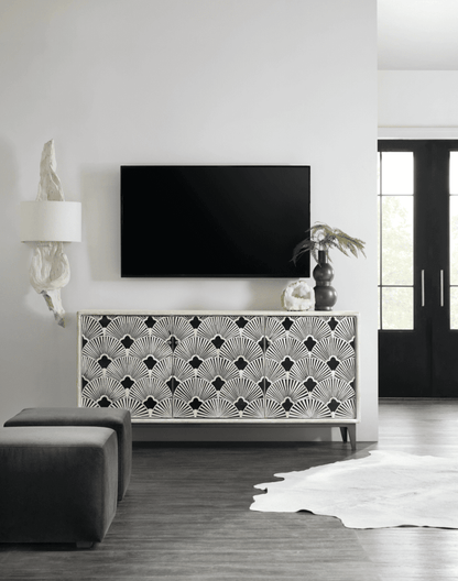Art deco bone inlay media console in black and white scalloped pattern, placed below a wall-mounted TV in a contemporary monochrome living room, flanked by a sculptural lamp and a dark ceramic vase with dried palm leaves