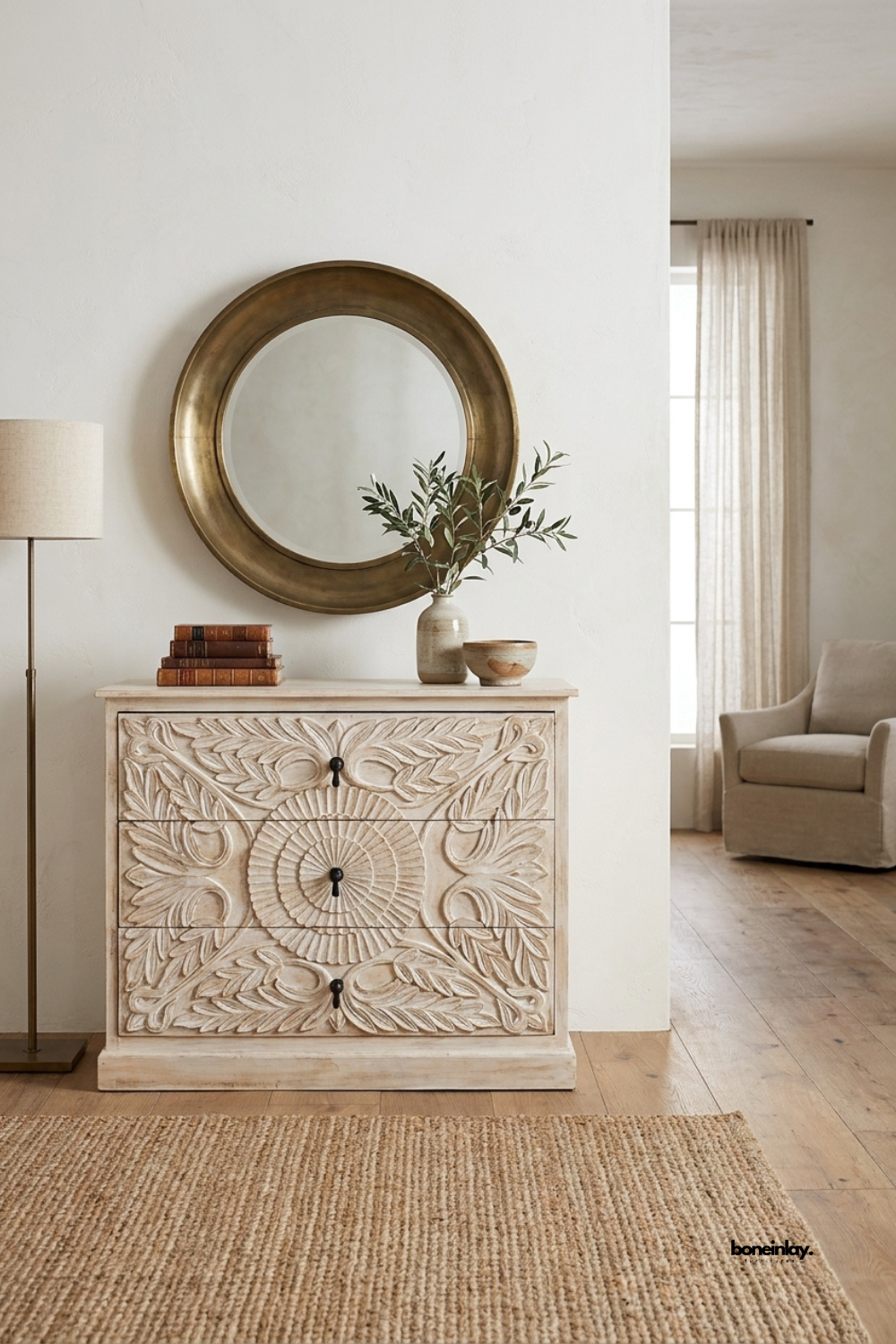 Hand-carved whitewashed wooden 3-drawer dresser featuring an ornate botanical rosette medallion relief across the drawer fronts and classic dark drop-pull hardware. Styled in a sunlit rustic bohemian room beside a clawfoot tub, exposed white brick wall, and woven floor rug, this artisan storage chest brings vintage charm and textural elegance to bedroom or bath interiors.