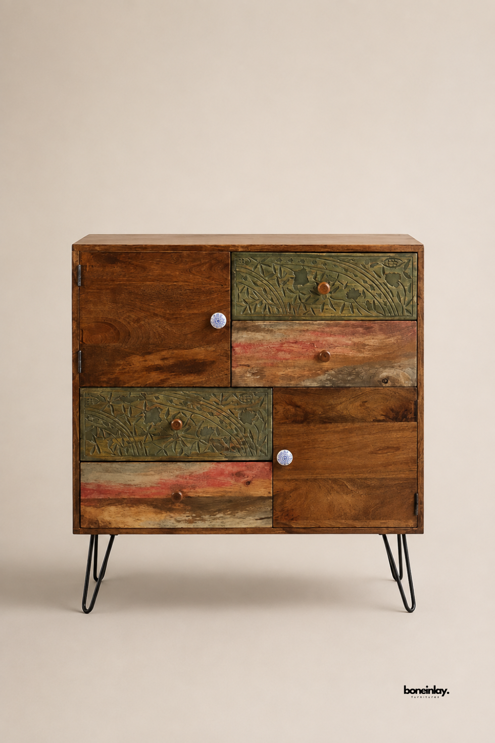 Reclaimed wood storage cabinet featuring a mixed-panel design with carved floral drawers, painted wood accents, and contrasting ceramic knobs. Set on sleek black hairpin legs for a modern industrial-boho look. Offers ample storage with one cabinet door and multiple drawers of varying sizes. A unique statement piece blending rustic textures with eclectic charm.