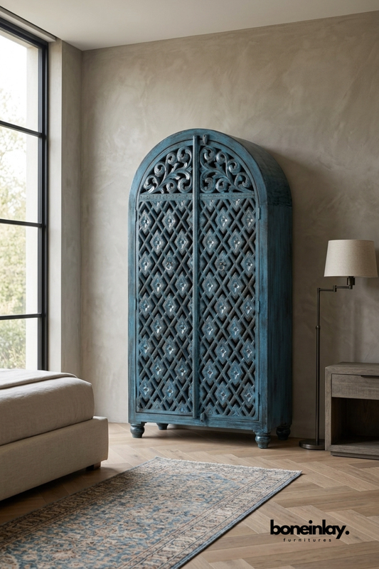 Blue arched wood armoire with a hand-carved diamond lattice pattern.
Rounded archway top features delicate carved vine scrollwork.
Distressed blue-grey finish gives it a vintage, weathered character.
Styled in a bedroom corner beside a floor lamp and patterned rug.
