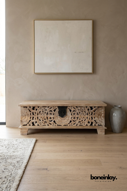 Rustic carved storage trunk in solid wood, styled in entryway beneath framed artwork, with floral relief and black latch.