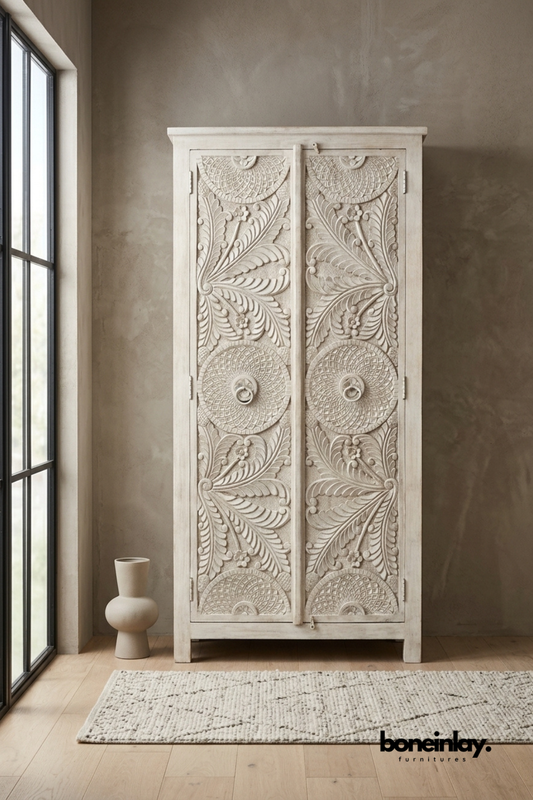 Tall whitewashed wood armoire with a hand-carved fan medallion pattern.
Symmetrical leaf and scallop carving repeats down both door panels.
Simple block legs ground the piece with a clean, minimal base.
Styled beside a sculptural ceramic vase near a black-framed window.