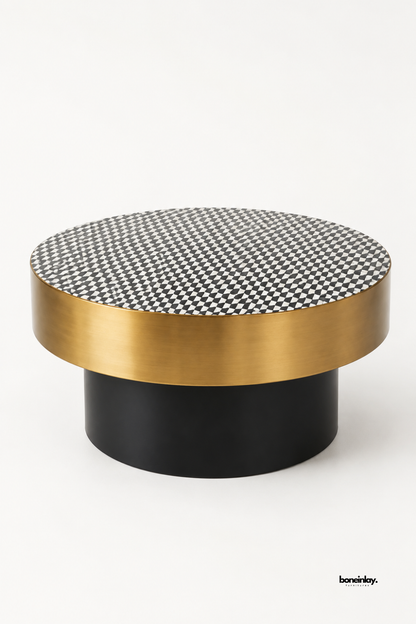 Artisan-crafted round coffee table featuring a monochrome black and white checkered bone inlay tabletop, a wide brushed brass metal apron band, and a matte black cylinder pedestal base. Showcased on a white studio background, this contemporary cocktail table seamlessly blends bold geometric art with modern metallic elegance.