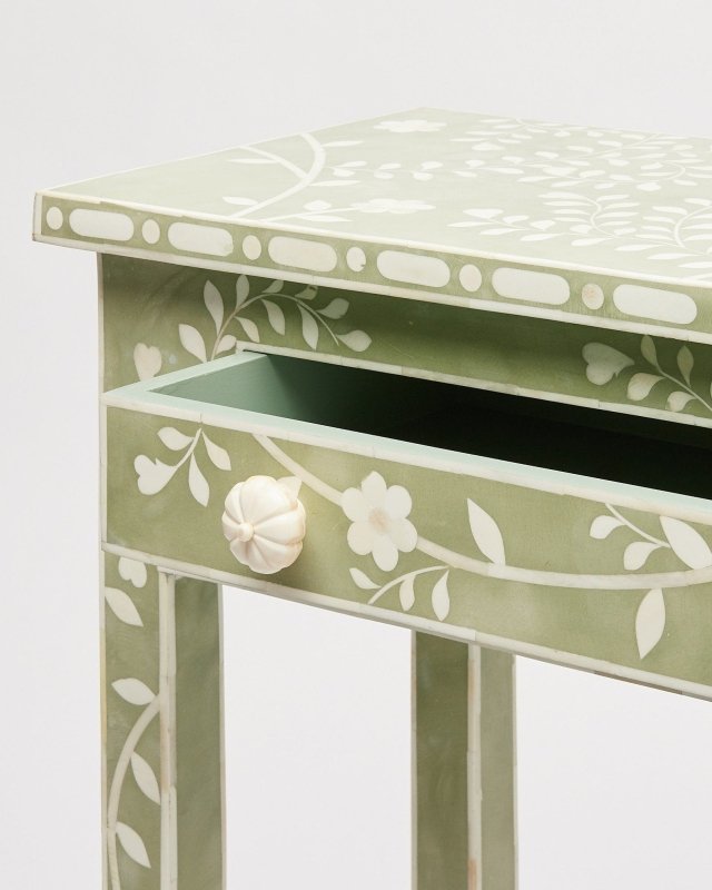 Open drawer detail of a sage green bone inlay console table showing carved bone flower knob and white vine inlay pattern on the drawer front and leg