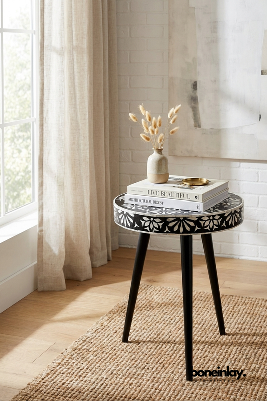 Handmade black and white bone inlay tripod side table with Pushkar floral motifs, styled with stacked books and a dried botanical vase on a jute rug in a bright living room setting.