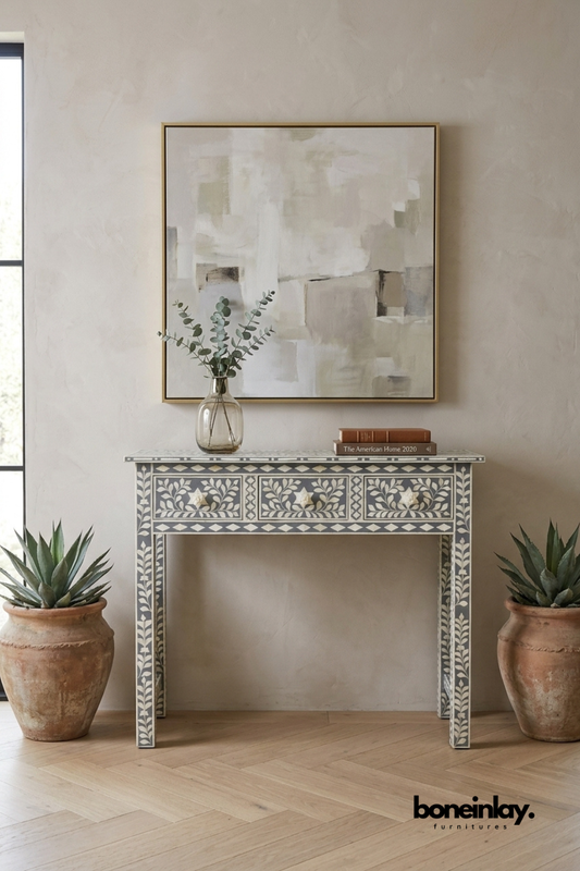 Grey and white bone inlay console table with a floral vine pattern.
Three drawers feature detailed leaf and flower inlay work.
Diamond border trim runs along the edges of the tabletop and legs.
Styled between two terracotta planters beneath a framed abstract print.