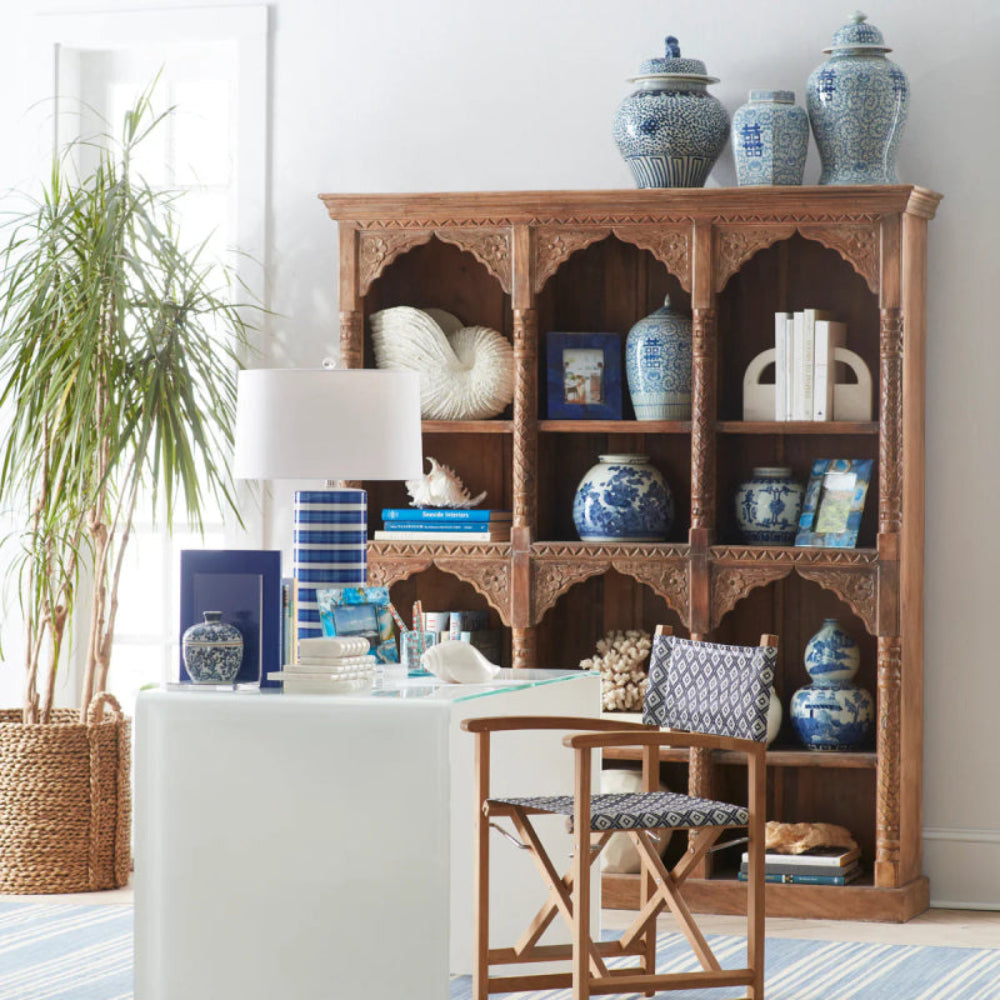 Brown wood display bookshelf, styled in living room with blue-and-white pottery, books and framed decor behind a desk.