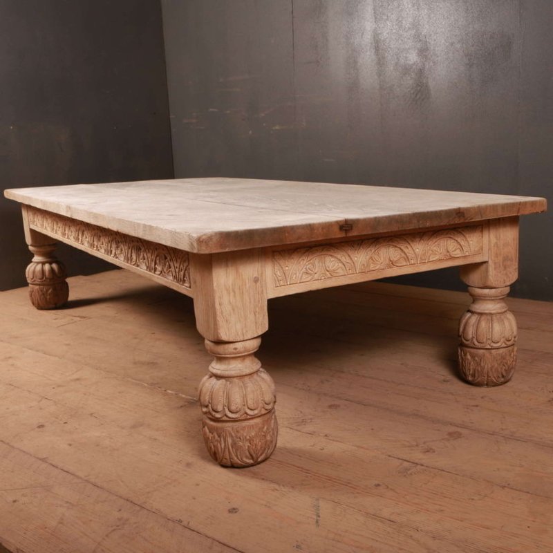Bulbous-leg wood coffee table with a carved apron and pale top, seen from a wider three-quarter angle on a wood floor.