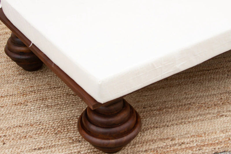Bun foot daybed in dark wood, shown in a close-up of the rounded leg beneath the white seat cushion.